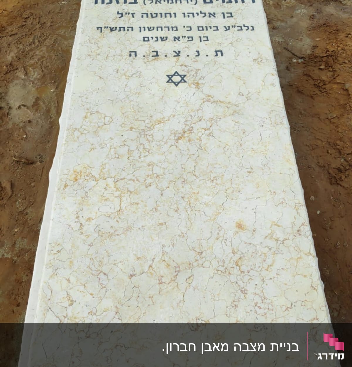 מצבה עם כיתוב בעברית ופרחים מסביב